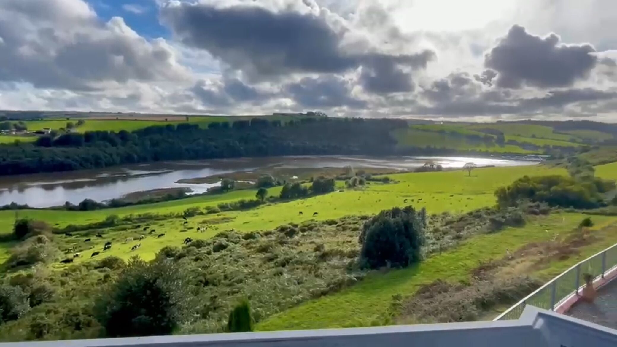 A river, green fields, and a cloudy sky.