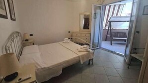 A bedroom with a bed, a nightstand, a dresser, a mirror, and a sliding glass door leading to a balcony. - Lights on the Sea (Alghero)