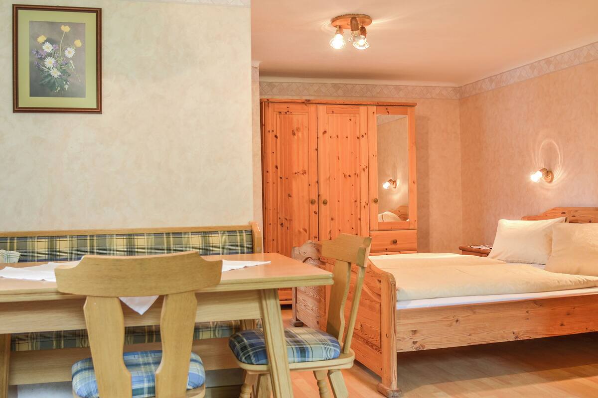 Ein Zimmer mit einem Holzbett, einem Holztisch mit zwei Stühlen, einer karierten Bank und einem gerahmten Bild an der Wand.