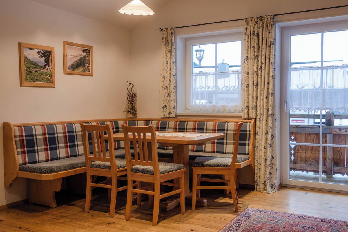 Ein gemütliches Zimmer mit einer hölzernen Bank, einem Tisch und Stühlen. An der Wand hängen zwei gerahmte Bilder.