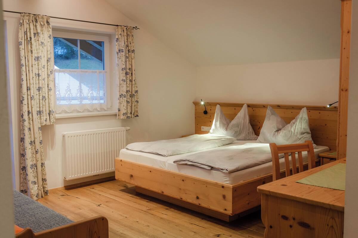 Ein hölzernes Bett mit weißer Bettwäsche in einem Zimmer mit Fenster und Heizkörper.