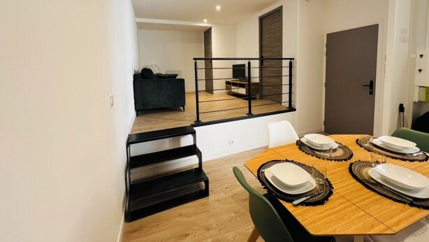 A modern dining area with a wooden table set for four, a staircase leading to a balcony, and a minimalist living space in the background. - CITY LOFT VALENCE HYPER CENTER (Valence)