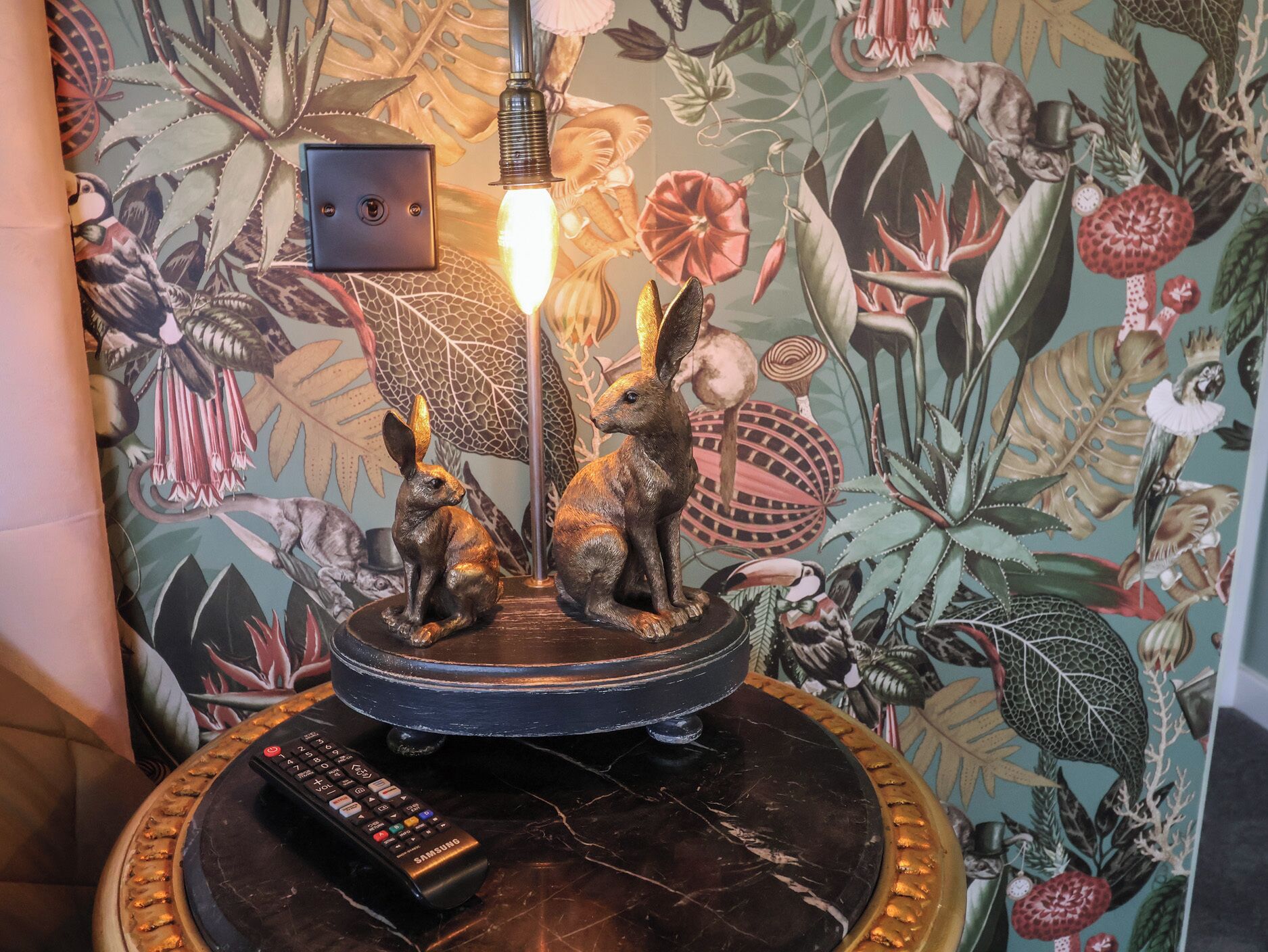 A decorative table with two rabbit figurines, a lamp, and a remote control.