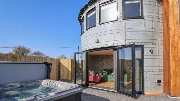 A modern building with a curved exterior, large sliding glass doors leading to an interior with a green sofa and a small table. - The Corn Silo (Ipswich)