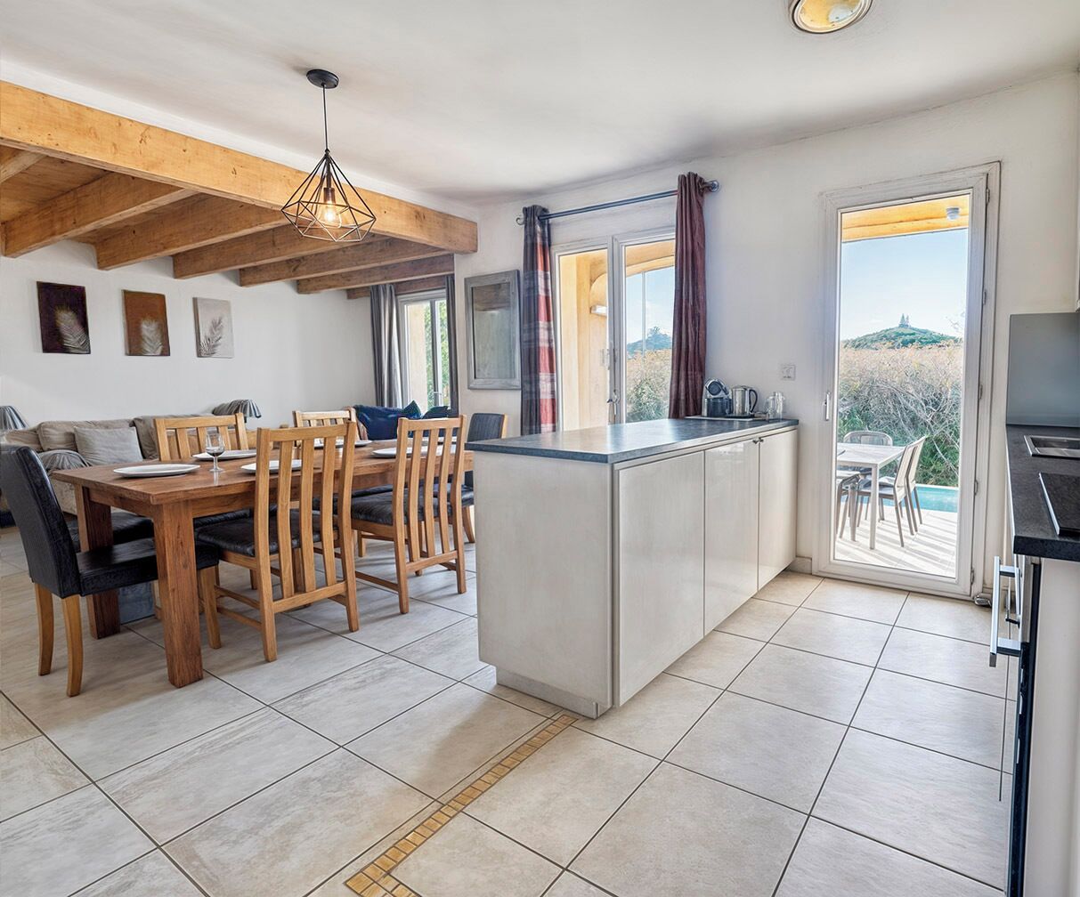 Cozinha moderna com ilha central, mesa de jantar de madeira e cadeiras. Uma janela grande oferece vista para o exterior.