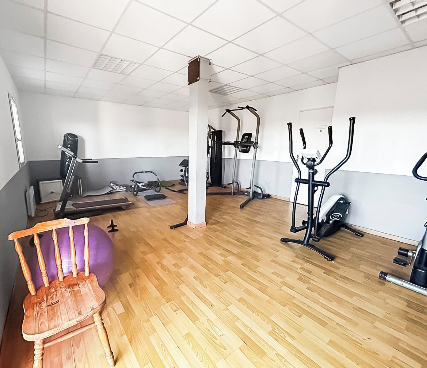 A gym with exercise equipment, a wooden floor, and a large window.