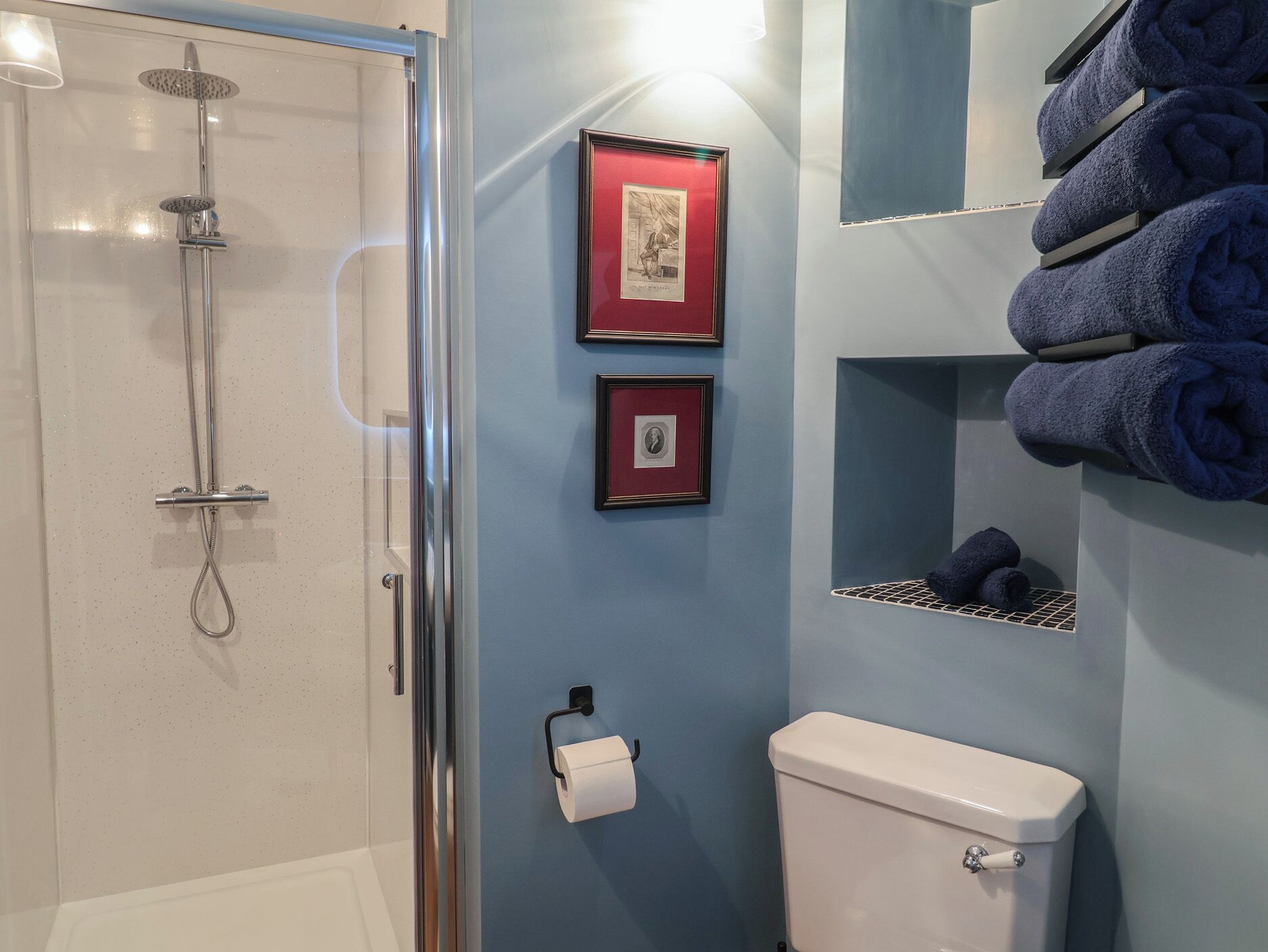 A bathroom with a glass shower enclosure, a toilet, and framed pictures on the wall.