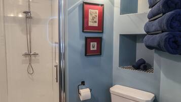 A bathroom with a glass shower enclosure, a toilet, and framed pictures on the wall.