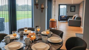 A dining area with a table set for breakfast, a view of the outdoors, and a living room in the background. - The Barley Silo (Ipswich)