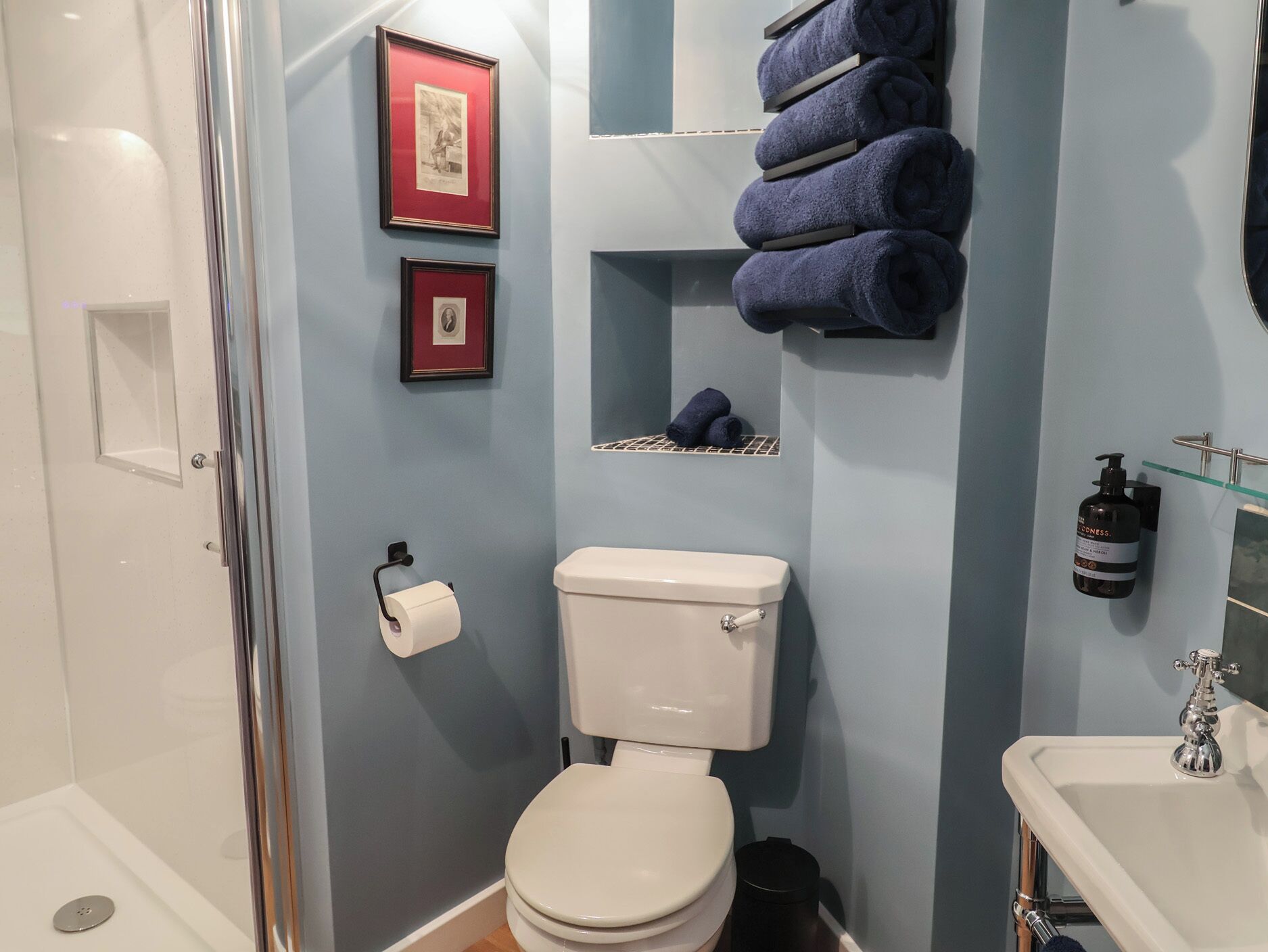 A bathroom with a toilet, a shower, and a sink. There are towels and a framed picture on the wall.