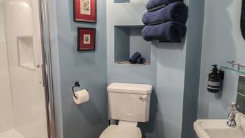 A bathroom with a toilet, a shower, and a sink. There are towels and a framed picture on the wall.