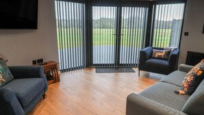 A modern living room with two sofas, a flat-screen TV, and large sliding glass doors leading to a grassy outdoor area. - The Barley Silo (Ipswich)