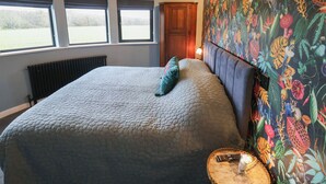 A bedroom with a large bed, a wooden headboard, a window, and a wall with a tropical print. - The Barley Silo (Ipswich)