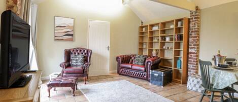 A cozy living room with a fireplace, leather armchairs, a sofa, and a bookshelf.