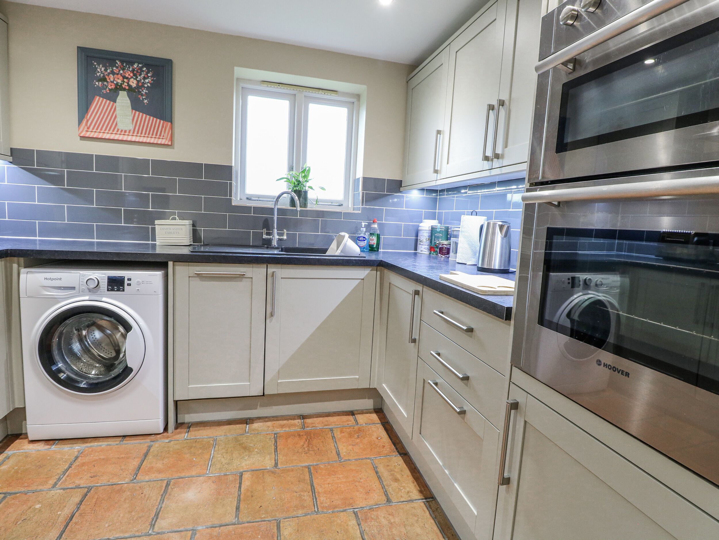 Een moderne keuken met een wasmachine, oven en een raam met een plant.