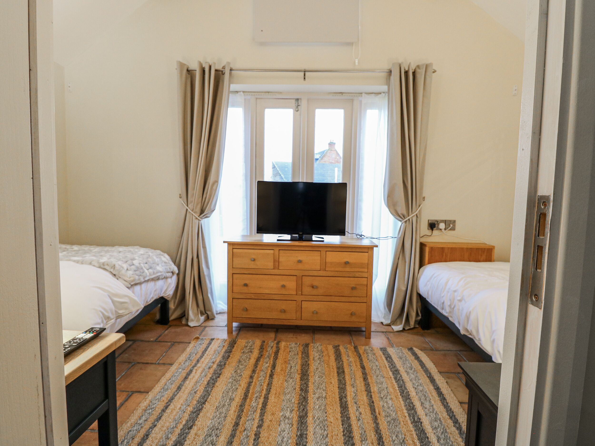 A bedroom with two beds, a wooden dresser, a television, and a window with curtains.