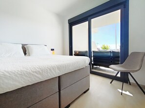A modern bedroom with a large bed, a chair, and a sliding glass door leading to a balcony. - Casa La Buena Vida by Sol Velapi Los Alcazares (San Javier)