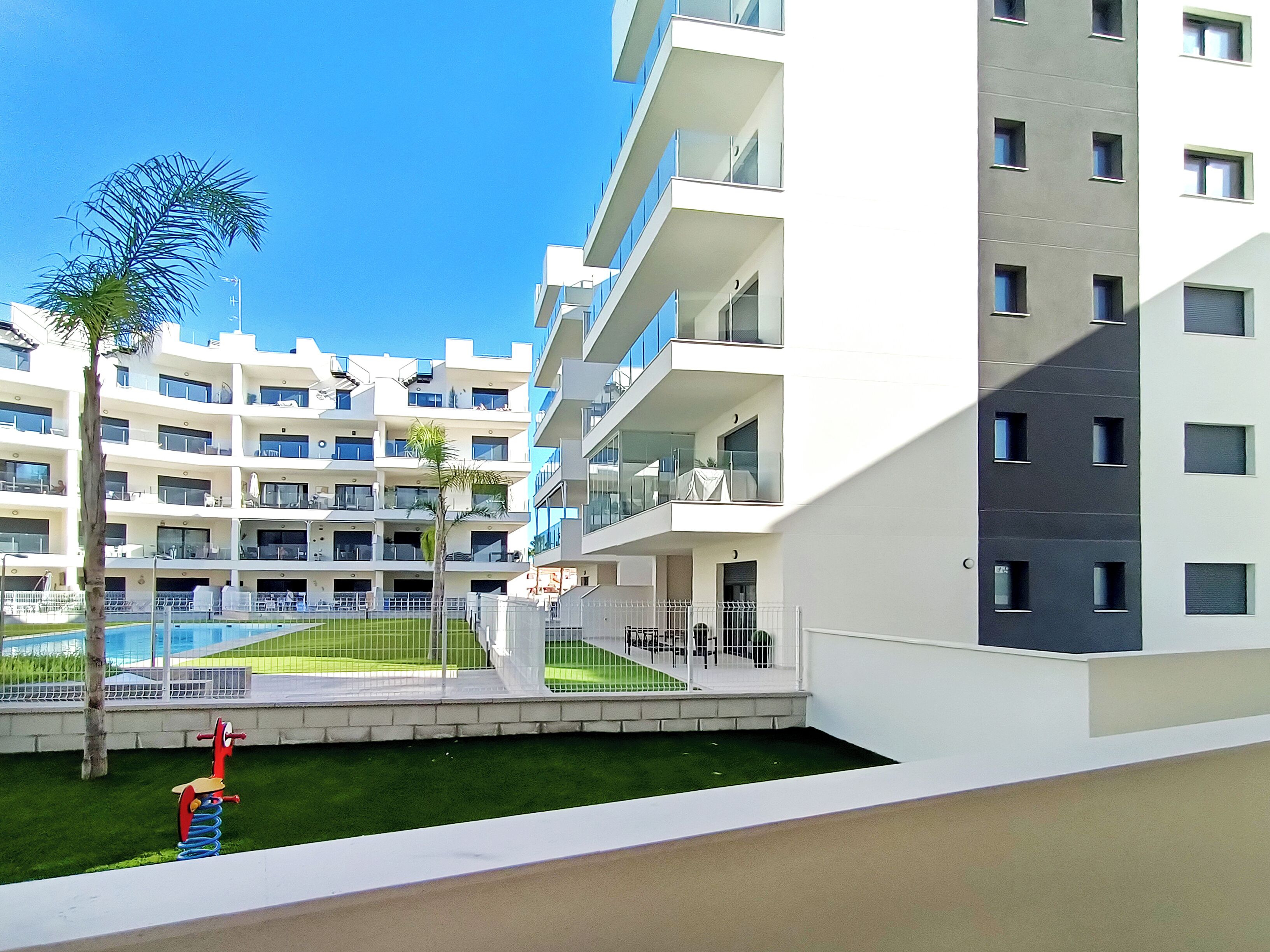 A modern apartment building with multiple balconies, a swimming pool, and a small playground area.