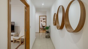 A hallway with a wooden door, a white chair, a desk with a TV, and a potted plant. - Carcavelos Bright Modern Apartment by Homing (Cascais)