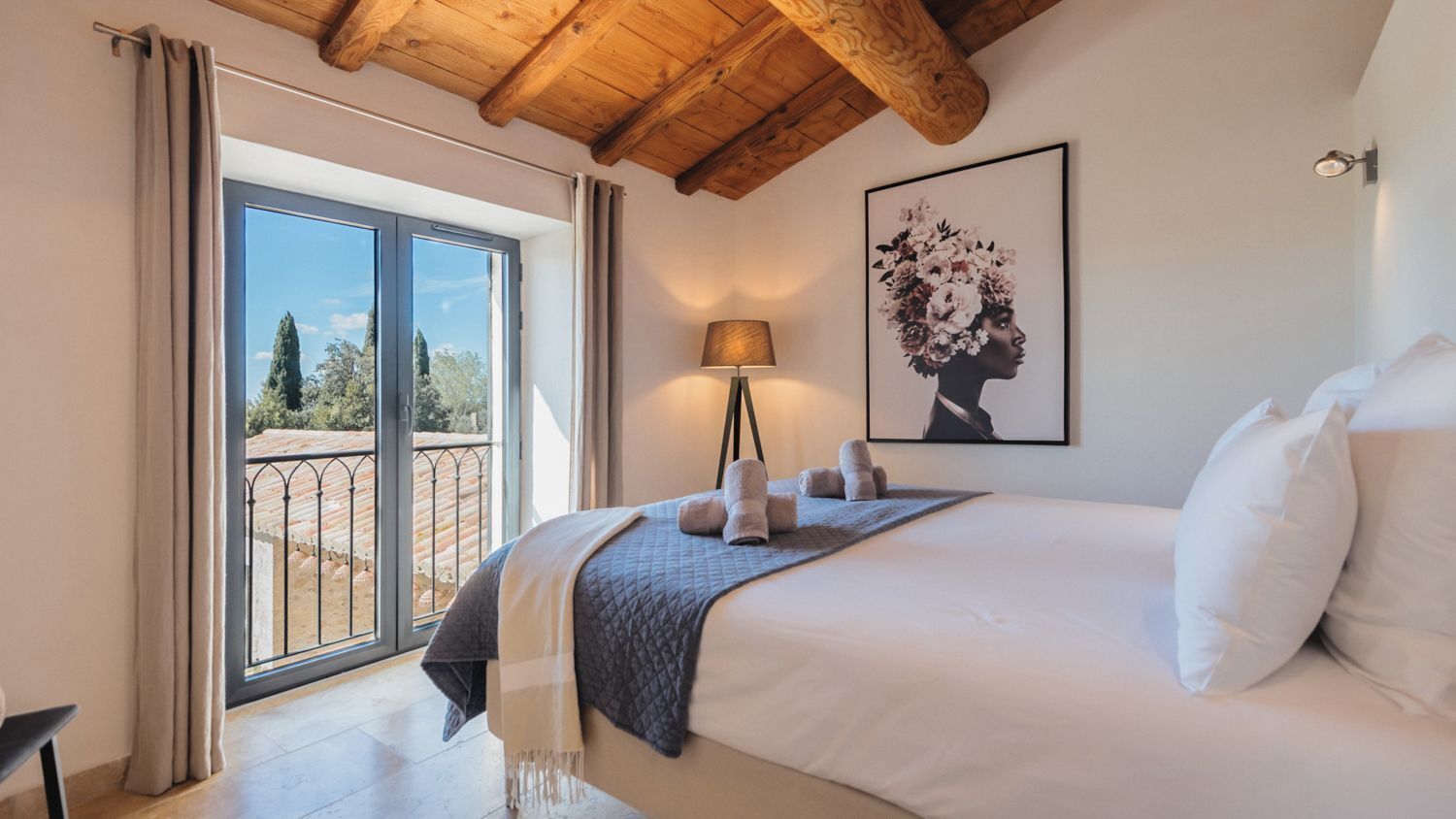 Un dormitorio con una cama grande, vistas a un espacio exterior por una puerta corrediza, una lámpara y un cuadro en la pared.