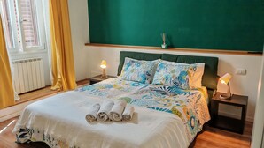 A neatly made bed with a floral bedspread, two pillows, and rolled towels on a wooden floor. - The Florence Nest (Firenze)