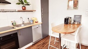 Eine kleine Küche mit Spüle, Herd und Schränken, einem Holztisch mit Stühlen und einem Blumentopf auf der Arbeitsplatte.