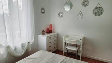 Une chambre à coucher comprenant un lit, une commode blanche, un bureau et des miroirs décoratifs fixés au mur.