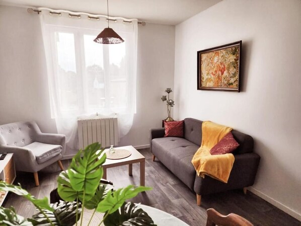 A living room with a grey sofa, a grey armchair, a coffee table, and a plant. - Cocon à Brocéliande & Ecoles militaires (Guer)
