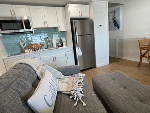 A modern kitchen with white cabinets, a stainless steel refrigerator, and a microwave. There is a blue tiled backsplash and a wooden chair in the dining area. - Beachfront with Balcony and Beach Chair Service (Panama City Beach)