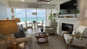 Een woonkamer met uitzicht op het strand, een plafondventilator, een open haard en een televisie.