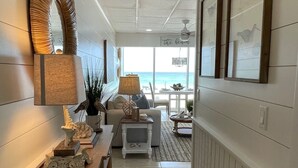 Een hal met uitzicht op de oceaan, een houten tafel met decoratieve objecten, een lamp en lijstjes met foto's aan de muren.