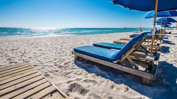 Een strand met houten ligbedden en blauwe parasols.