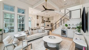A spacious living area with a high ceiling, a modern kitchen, and a staircase leading to an upper level. - Stylish Laid-Back Escape: Community Pool, 6 Bikes, & Spacious 3 Story Layout (Seagrove Beach)
