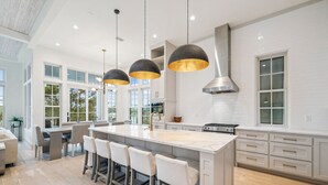 A modern kitchen with a large island, pendant lights, and a view of the outdoors. - Stylish Laid-Back Escape: Community Pool, 6 Bikes, & Spacious 3 Story Layout (Seagrove Beach)