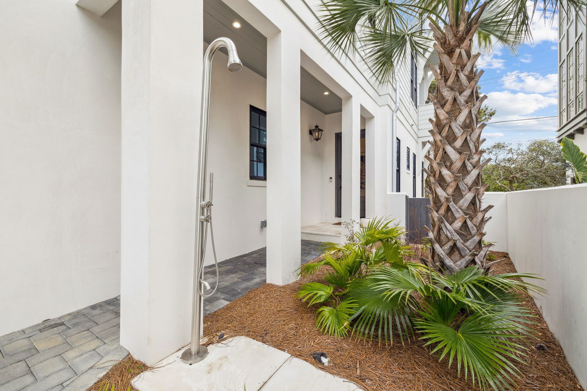 A covered outdoor area with a shower, palm trees, and a stone-tiled floor.