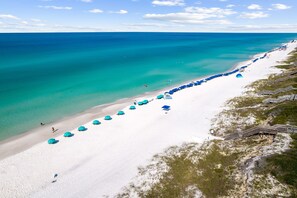 An aerial view of a beach with a long row of blue umbrellas and a wooden walkway leading to a beach area. - Stylish Laid-Back Escape: Community Pool, 6 Bikes, & Spacious 3 Story Layout (Seagrove Beach)