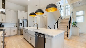 A modern kitchen with white cabinetry, stainless steel appliances, and a central island. - Stylish Laid-Back Escape: Community Pool, 6 Bikes, & Spacious 3 Story Layout (Seagrove Beach)