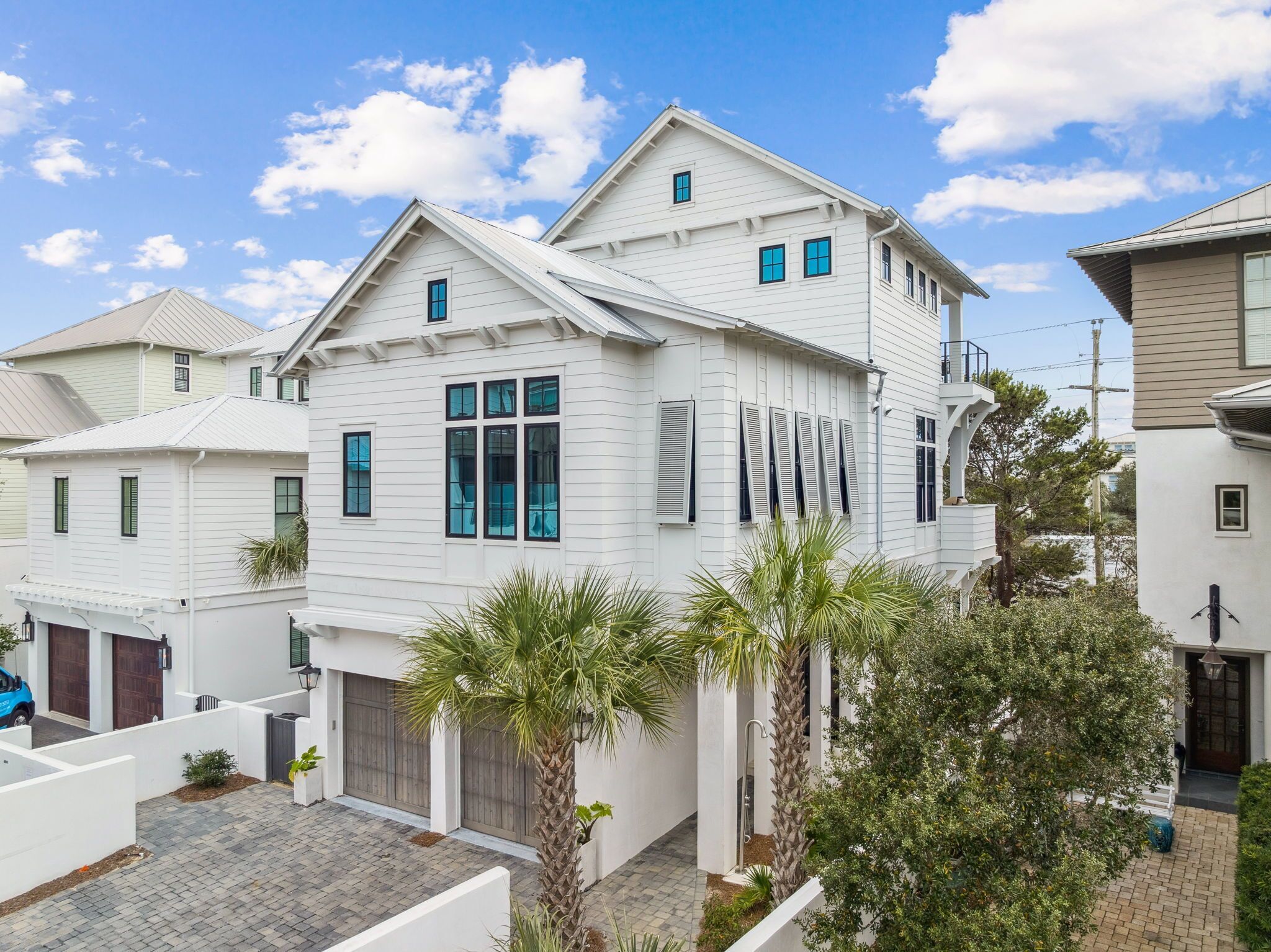 A white two-story house with a garage, a covered patio, and a small garden with palm trees.