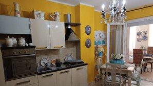 Una cucina con mobili bianchi, un fornello e un lavello. Sulle pareti sono presenti piatti decorativi e un lampadario sopra il tavolo da pranzo.