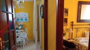 Una stanza con un letto, una poltrona, un tavolo con sedie, una sveglia e un lampadario.