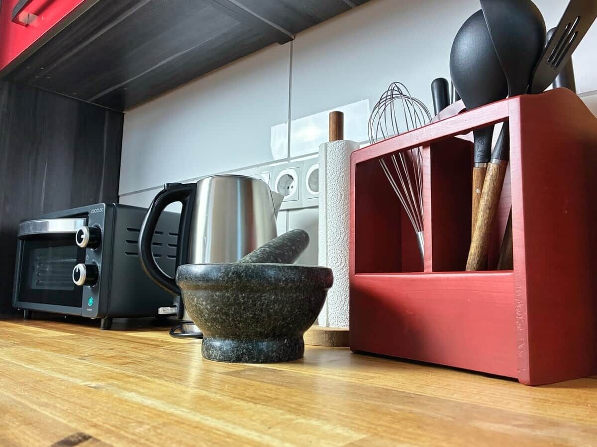 Une cuisine équipée d’un four à micro-ondes, d’un grille-pain, d’une bouilloire et d’un porte-épices rouge contenant des ustensiles.