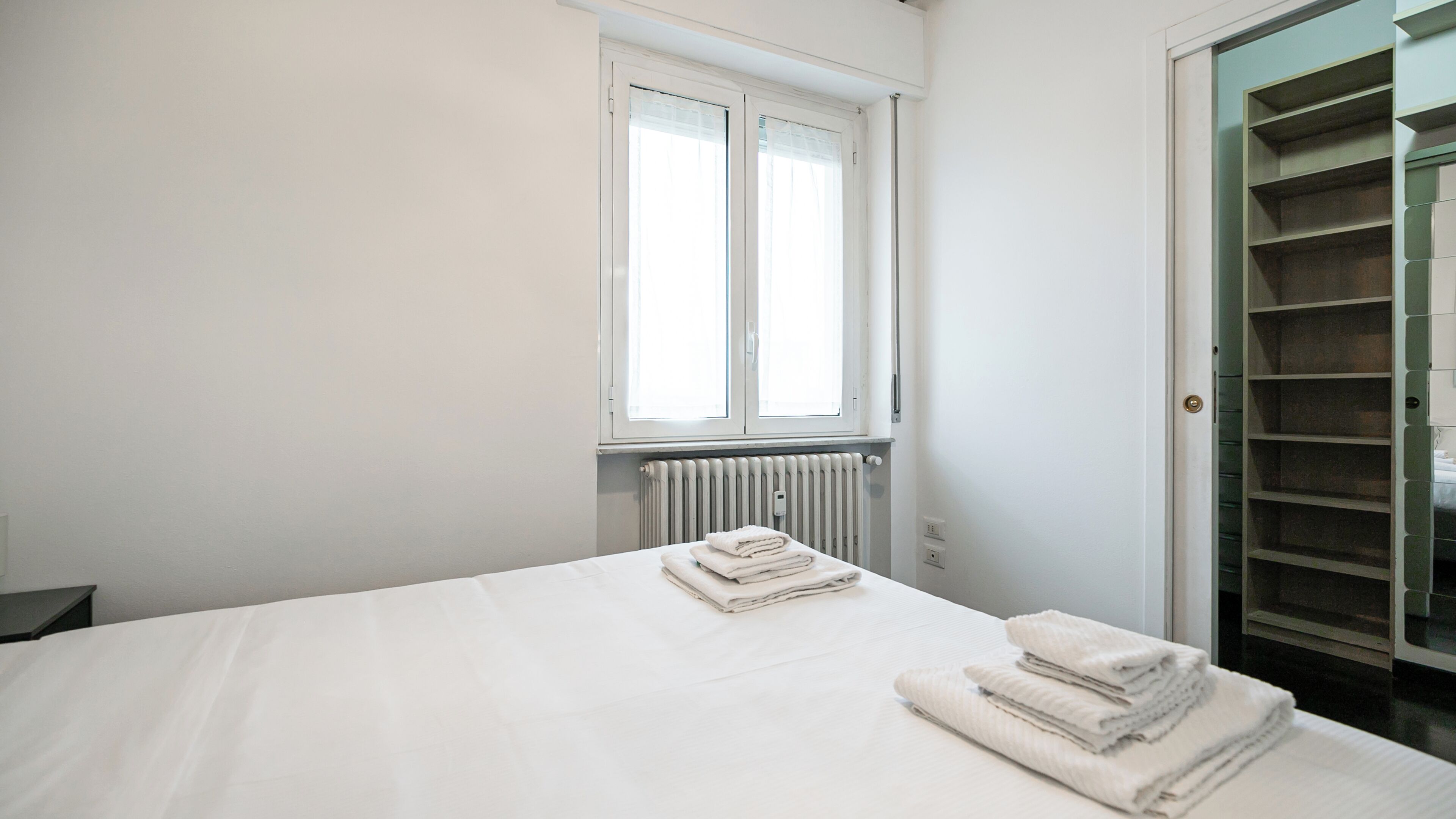 Une chambre à coucher avec un lit, un radiateur, une fenêtre et un placard.