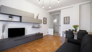 Un salon moderne doté d’un téléviseur à écran plat, d’un meuble de rangement gris foncé, d’un plancher en bois et d’un coin repas avec une table et des chaises.