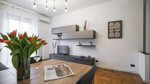 Un salon moderne avec une table à manger en bois, un vase de tulipes, un verre de vin et un téléviseur à écran plat posé sur un meuble sombre.
