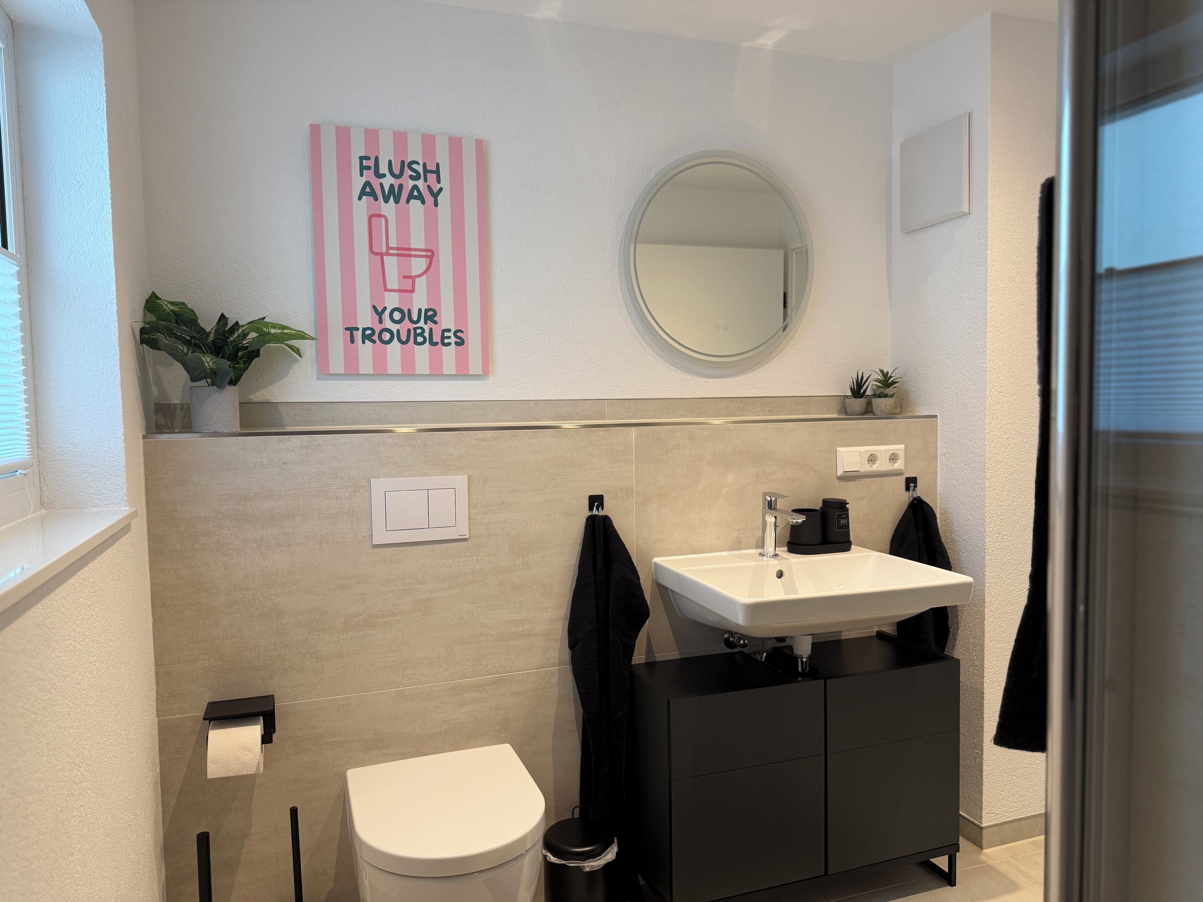 Une salle de bain avec des toilettes, un lavabo et un miroir. Au-dessus du lavabo, on peut lire l’inscription suivante : « ÉVACUEZ VOS SOUCIS DANS LES TOILETTES ».