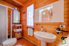 A wooden cabin bathroom with a toilet, sink, and a shower area. - Hotiday Pragelato (Pragelato)