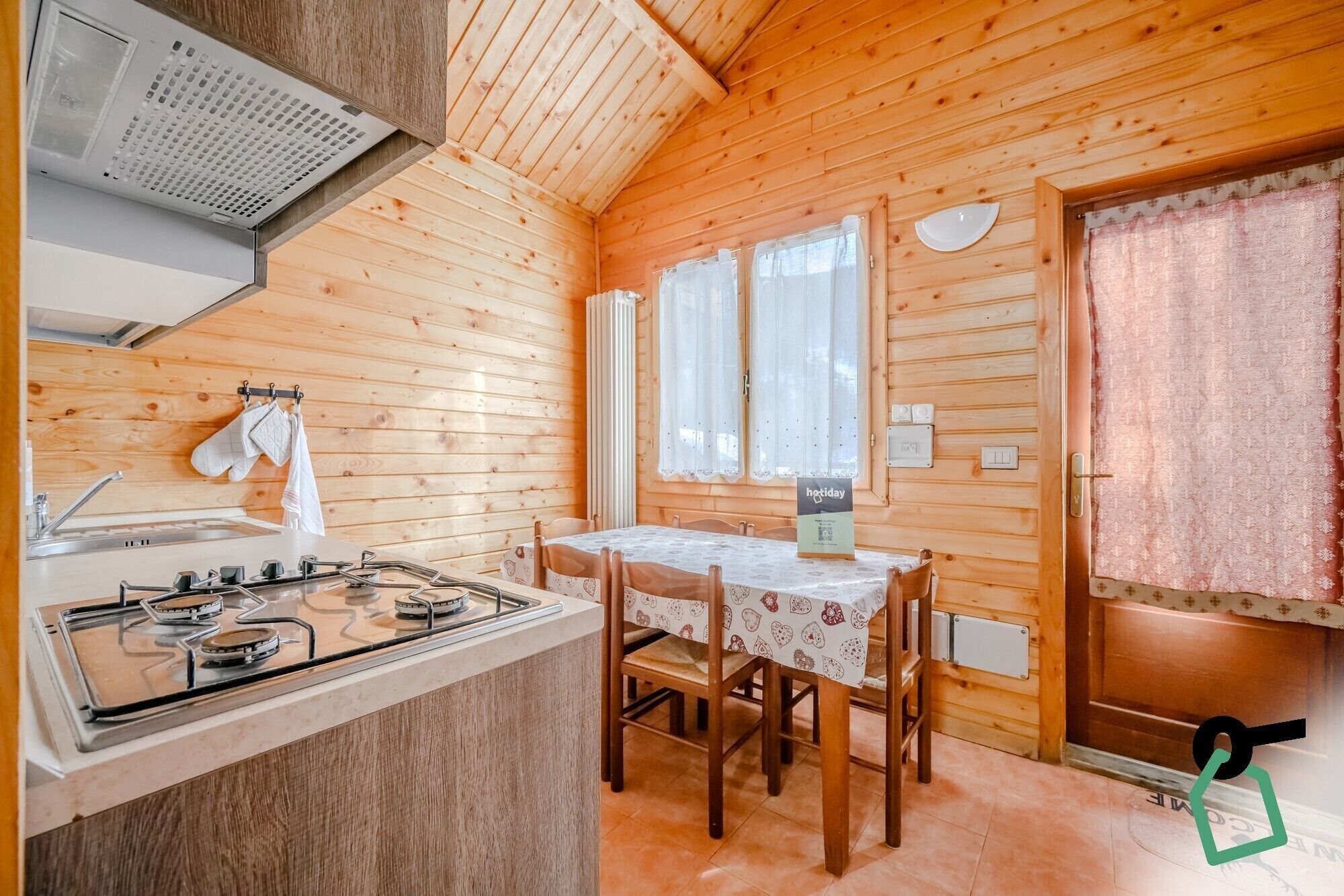 Une cabane en bois dotée d’un coin cuisine comprenant une cuisinière à gaz, un évier et une table à manger avec des chaises.