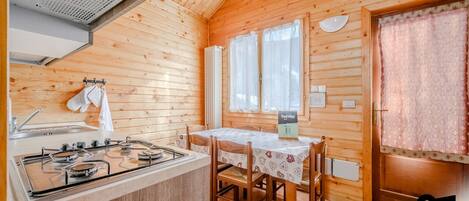 Una cabaña de madera con una zona de cocina que incluye una estufa a gas, un fregadero y una mesa de comedor con sillas.