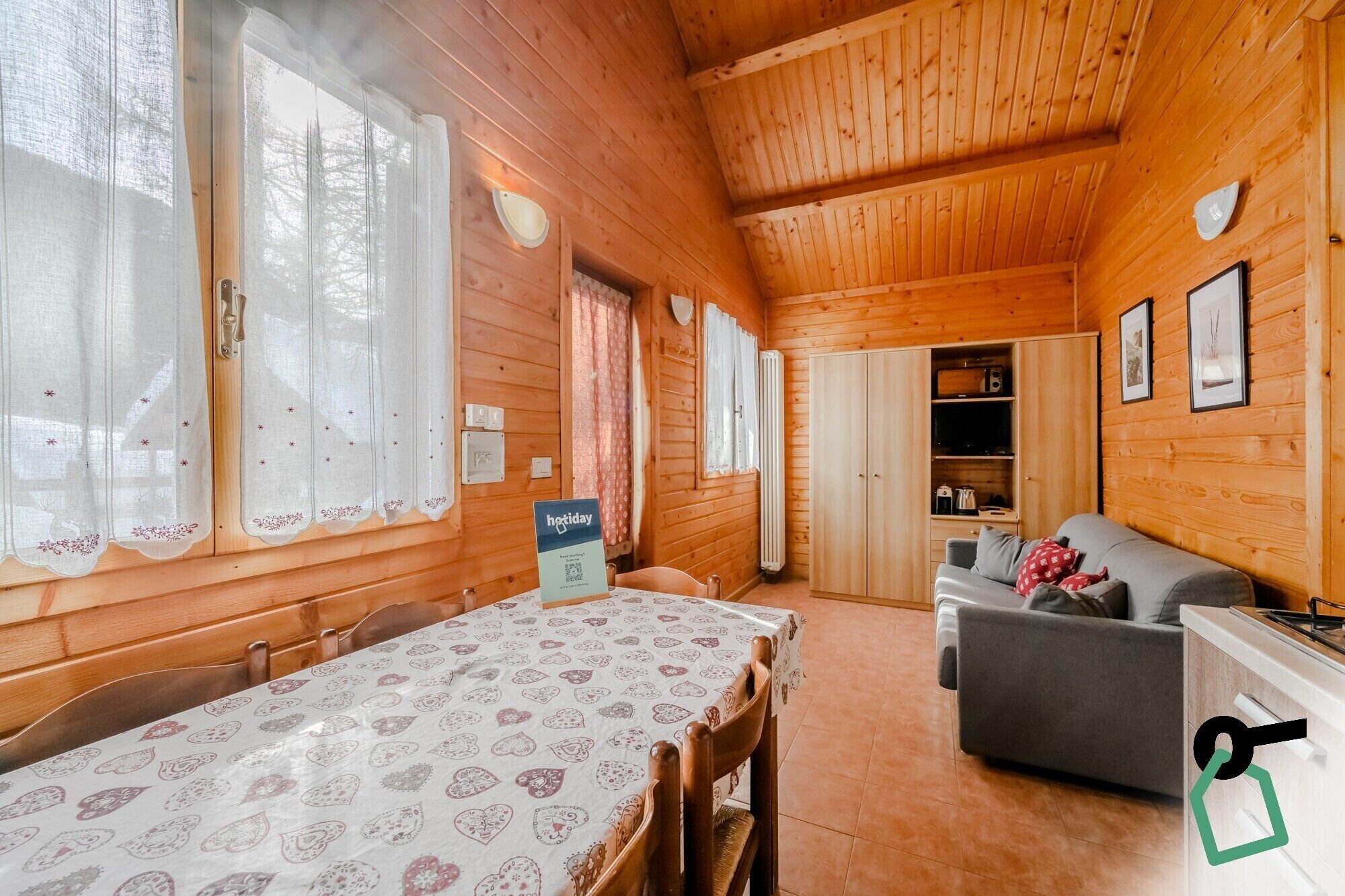 A cozy cabin interior with a dining table, chairs, a sofa, and a kitchenette.