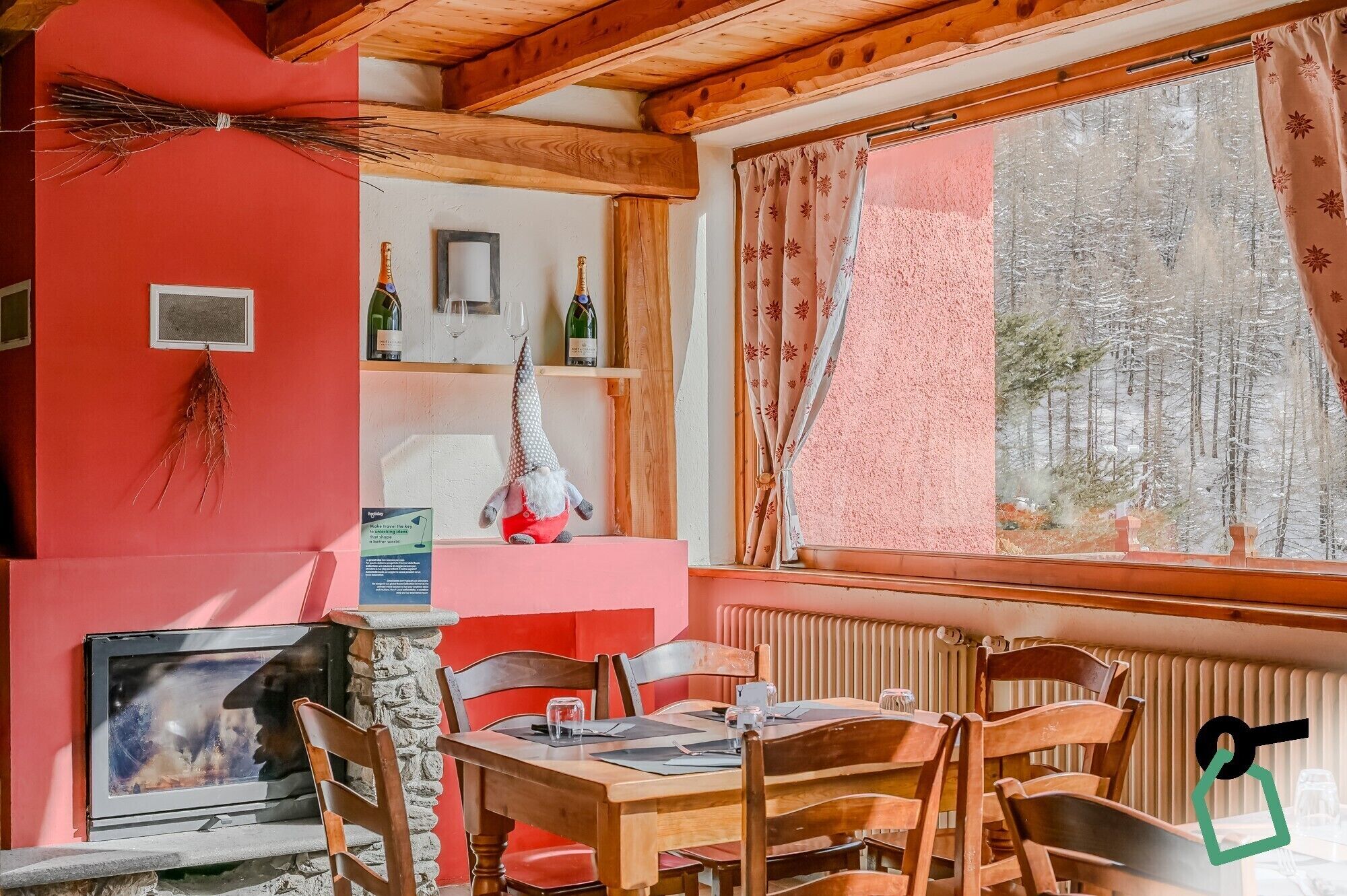 Un'accogliente sala da pranzo con mobili in legno, un camino in pietra e una finestra vista su una foresta innevata.
